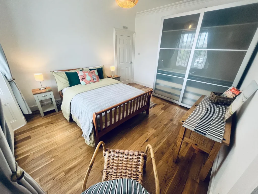 Cozy bedroom with wooden bed, soft lighting, and modern decor, featuring sliding wardrobe and wooden floor.