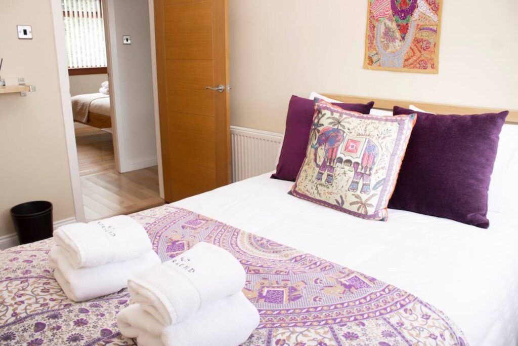 Cozy bedroom with elephant-themed decor and plush purple pillows, featuring folded white towels on the bed.