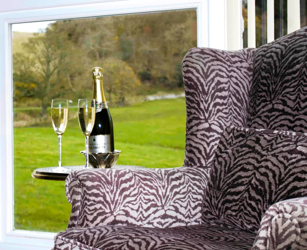 Zebra-patterned chair with champagne and glasses by a countryside window. Luxurious comfort in a scenic setting.