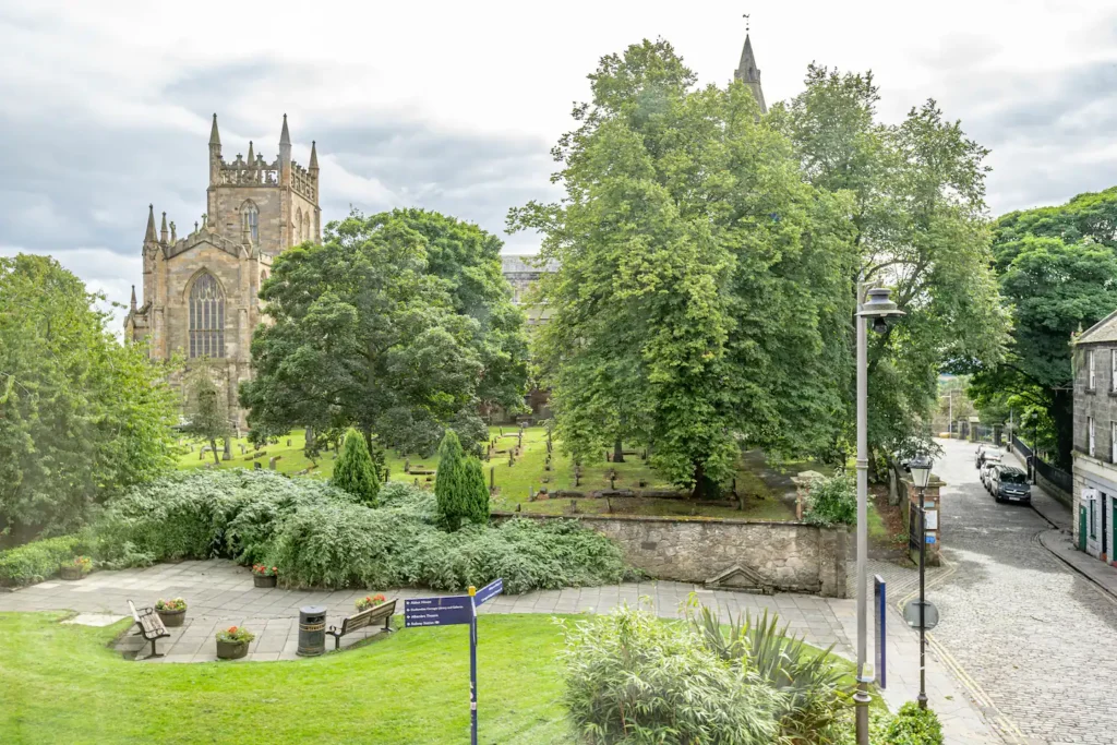 Historic stone church surrounded by lush trees and cobblestone path on a cloudy day.