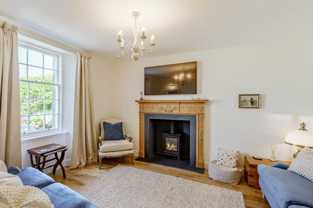 Cozy living room with elegant fireplace, blue sofa, armchair, and large window with curtains.