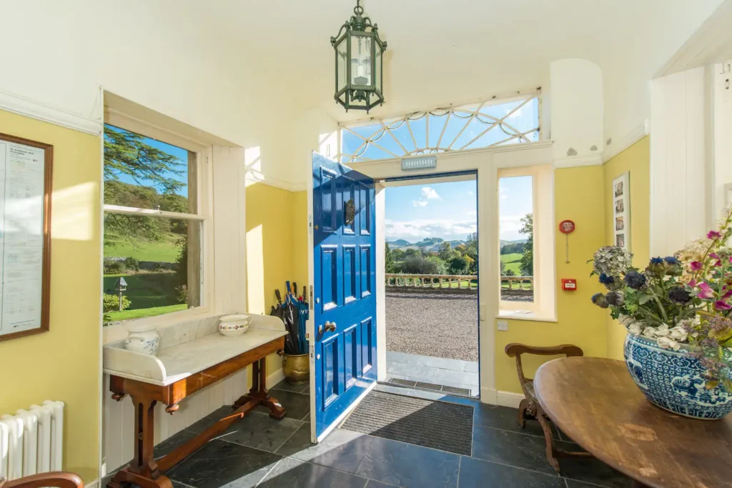 Bright entry with blue door, vibrant yellow walls, elegant decor, and scenic countryside view.