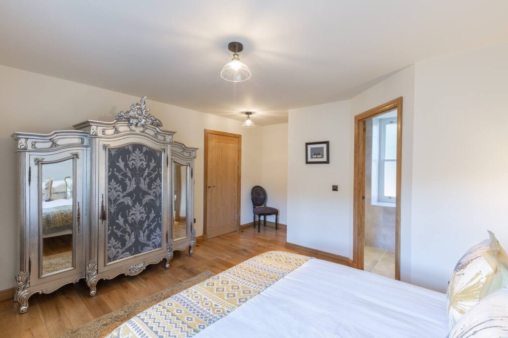 Elegant bedroom with ornate wardrobe, cozy bedding, and warm wood accents; bright and inviting interior design.