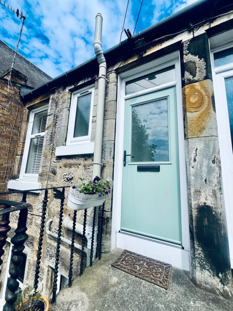 Old stone house with a light blue door and potted flowers, set against a clear blue sky.