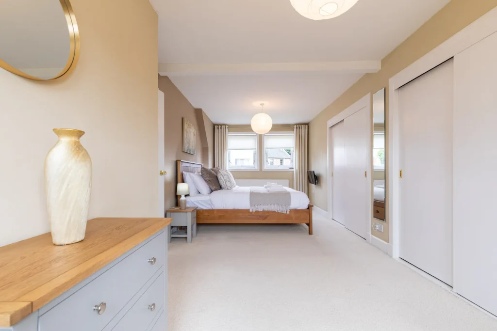 Modern bedroom with neutral tones, wooden bed, and stylish decor, featuring large windows and ample natural light.