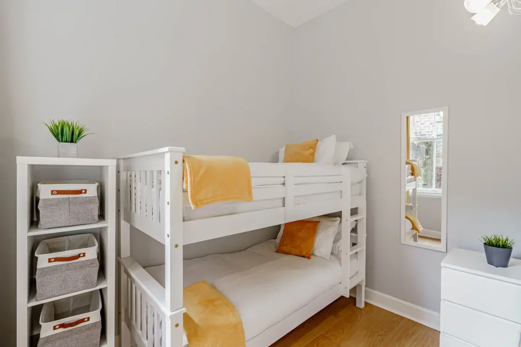 White bunk beds in a cozy kids' room with yellow accents and storage shelves. Modern design with natural light.