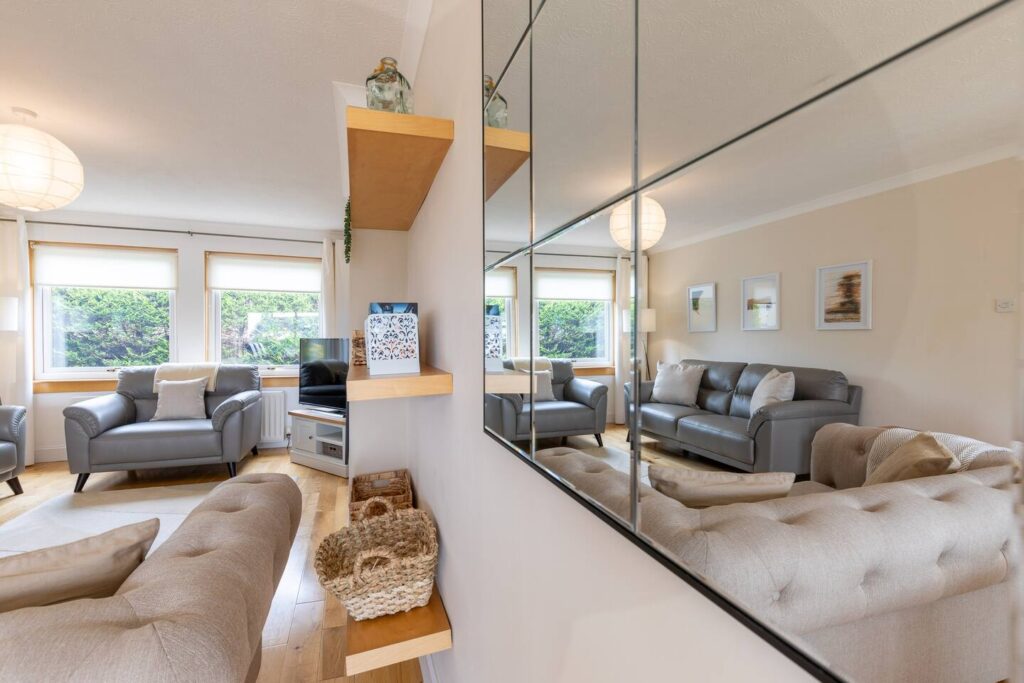 Cozy modern living room with grey sofas, large windows, and a mirror reflecting the bright, airy space.