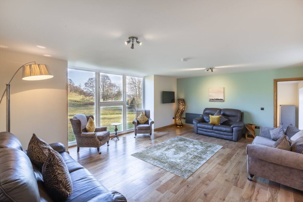 Modern living room with large windows, cozy seating, and scenic view. Bright and inviting interior design.