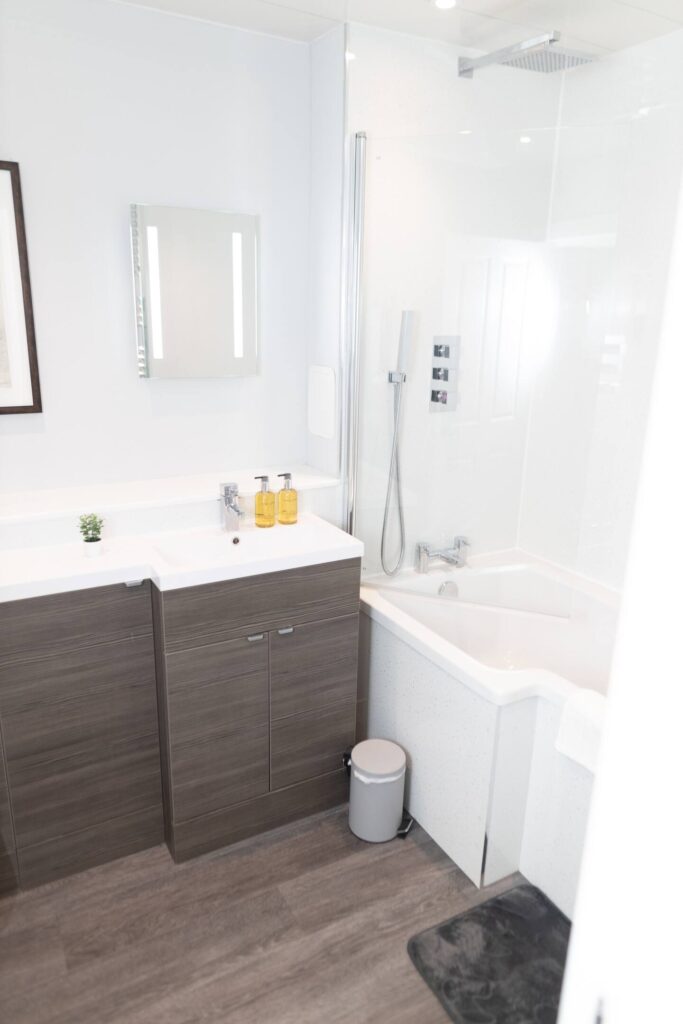 Modern bathroom with white fixtures, wood cabinets, corner bathtub, and wall-mounted showerhead.