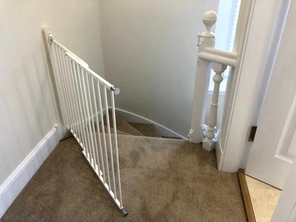 Child safety gate installed at the top of carpeted stairs in a home, ensuring stairway security.