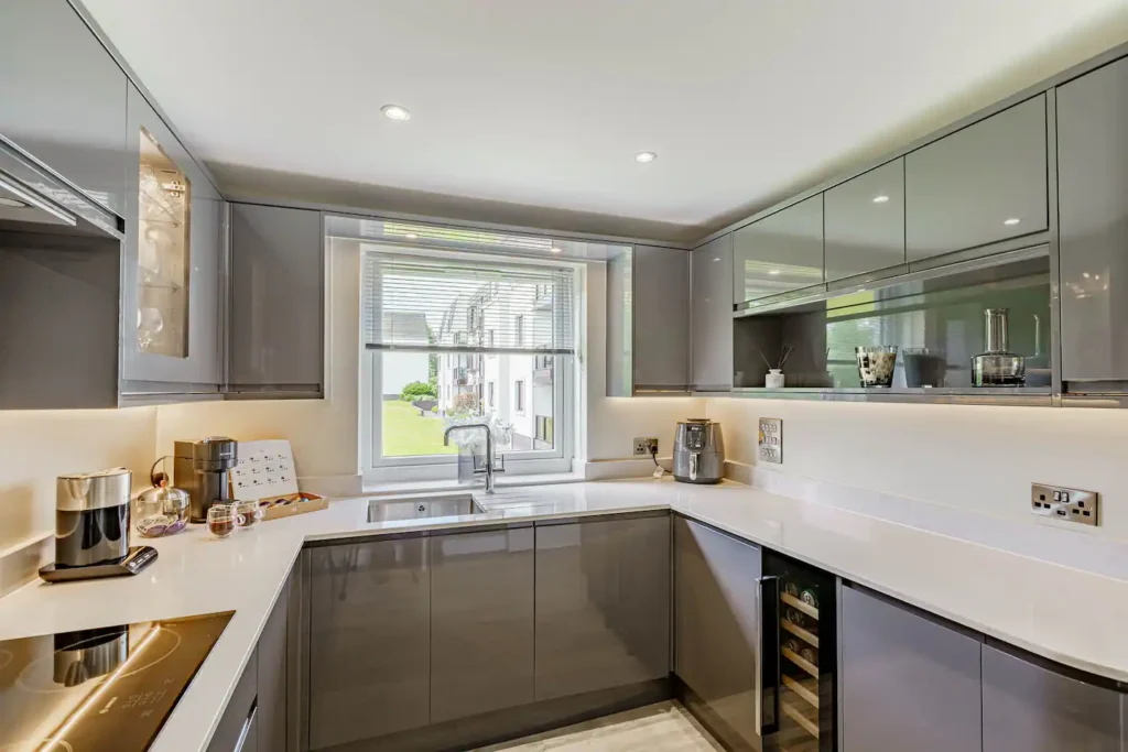 Modern kitchen with sleek grey cabinets, white countertops, and bright natural light from the window.