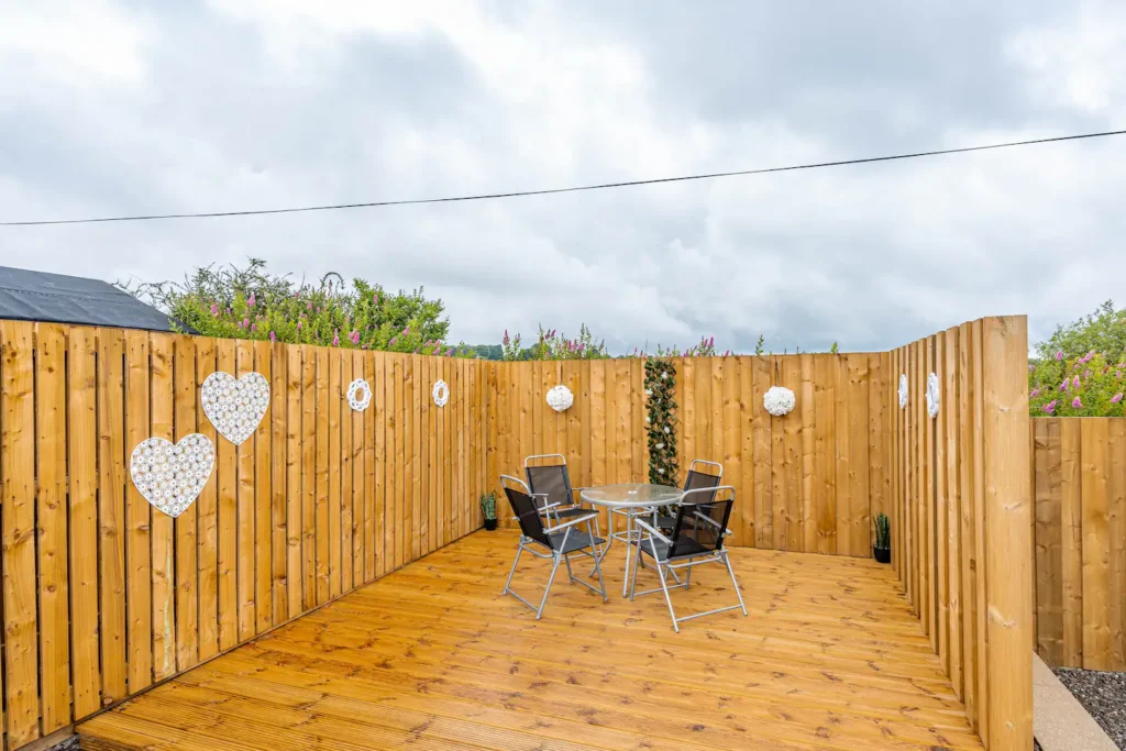 Outdoor patio with wooden fence, heart decor, and glass table with chairs under a cloudy sky.