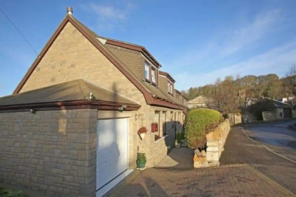 Beautiful stone house with a sloped roof and lush greenery on a sunny day. Charming residential architecture.