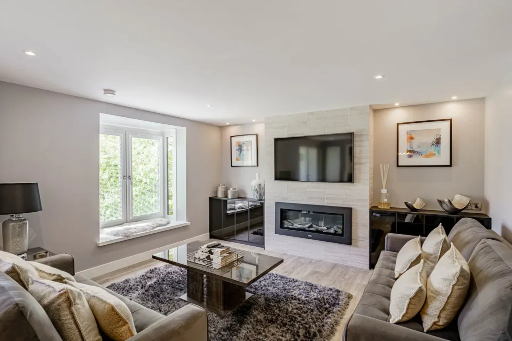 Modern living room with cozy sofas, a sleek fireplace, large TV, and stylish decor. Natural light through a window bench.