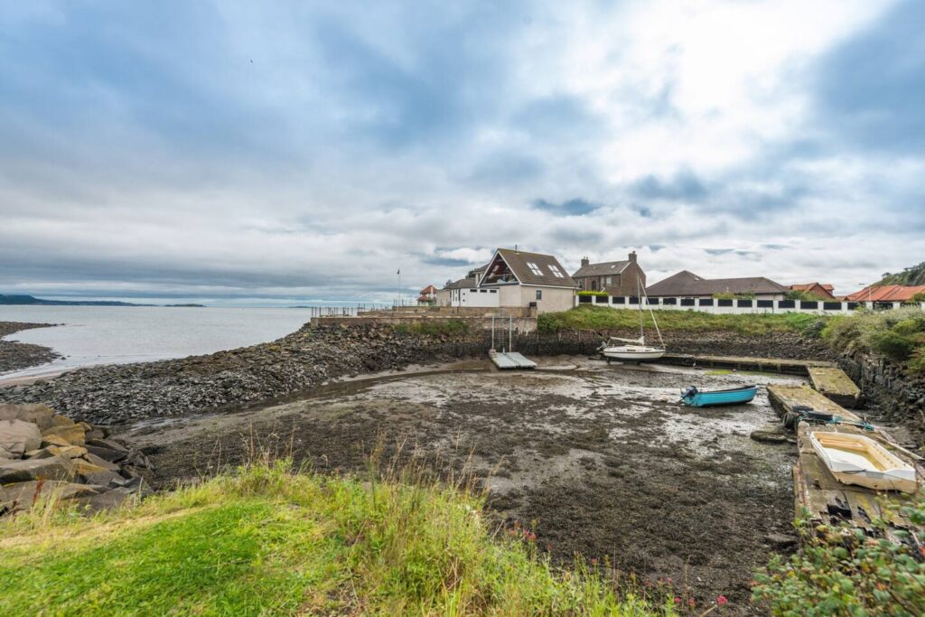 Coastal village with boats in a small harbor, rocky shoreline, and cloudy sky.