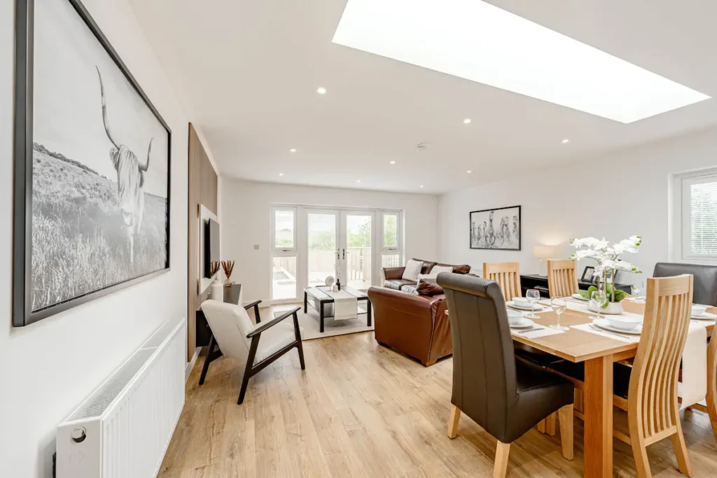 Modern open-plan living and dining room with stylish decor, large windows, and a cozy seating area.