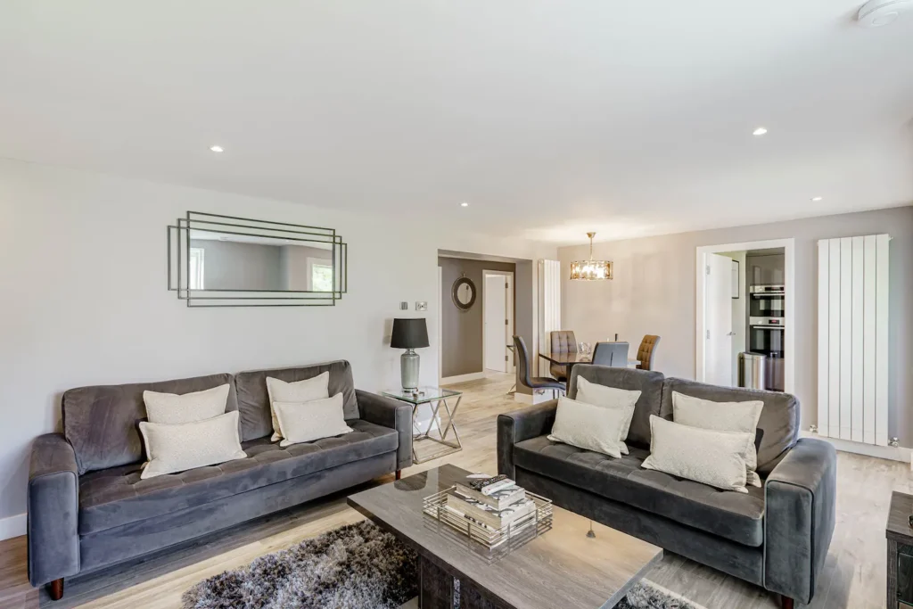 Modern living room with gray sofas, glass coffee table, and dining area in stylish, open-concept home.