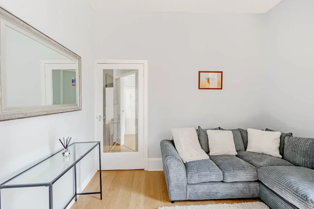 Modern living room with gray sectional sofa, decorative cushions, wall mirror, and minimalistic decor.