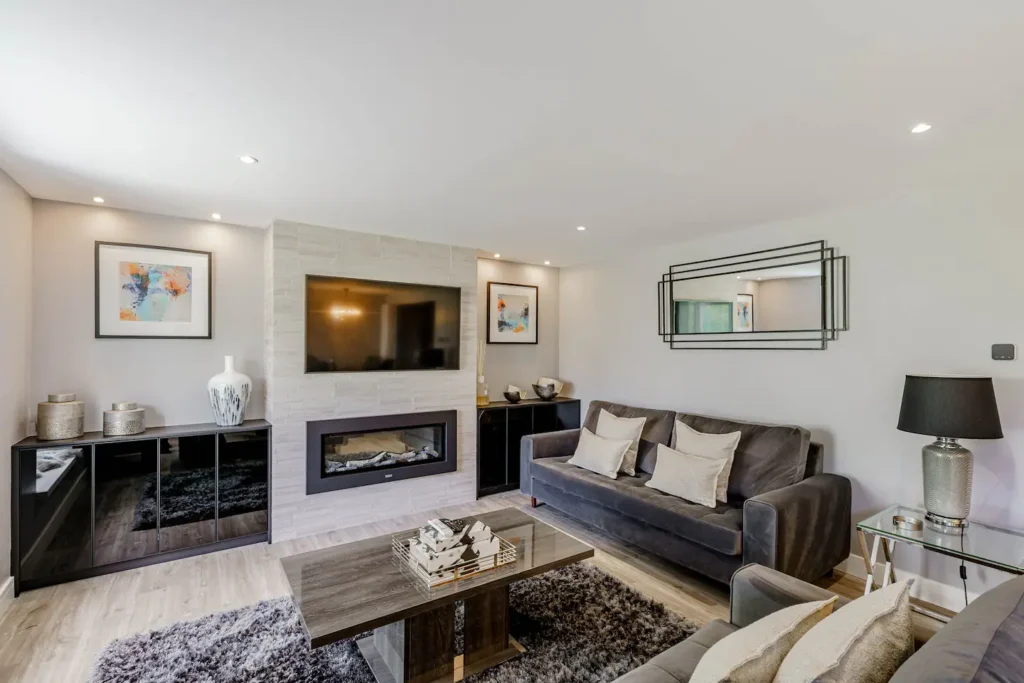 Modern living room with gray sofa, wall-mounted TV, fireplace, rug, and decorative elements. Cozy and stylish interior.