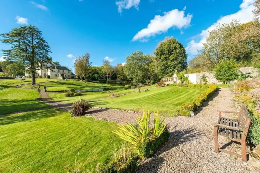 Expansive green garden with trees, pathways, and a bench under a clear blue sky.