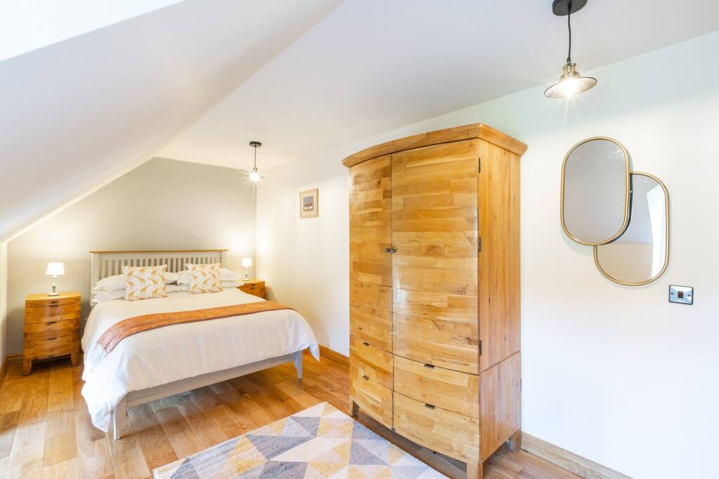 Bright and cozy bedroom with wooden furniture, double bed, and modern mirrors.