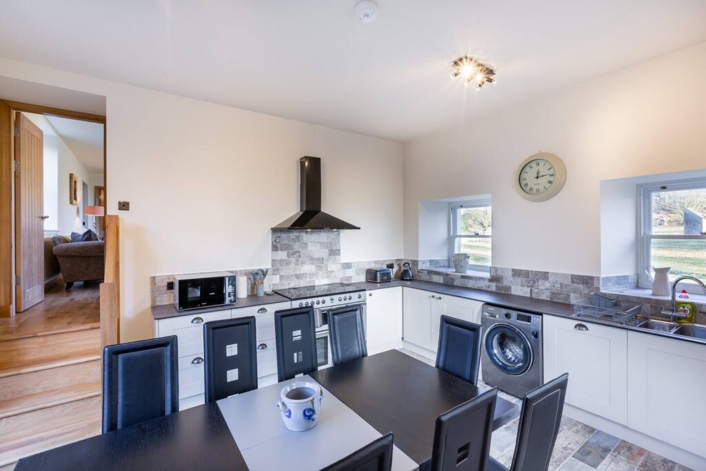 Modern kitchen with dining table, black chairs, washing machine, and stylish tile backsplash under bright lighting.