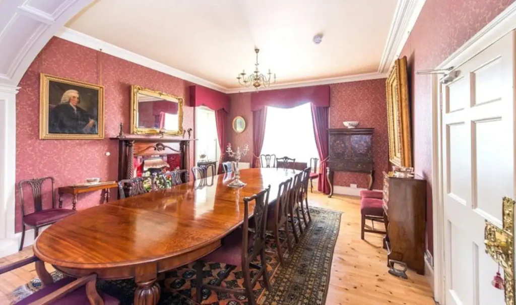 Elegant vintage dining room with polished wood table, classic chairs, ornate mirrors, and pink wallpaper.