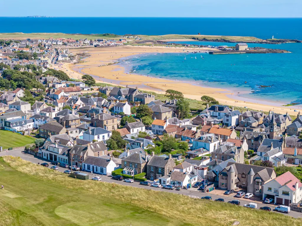 Scenic coastal town with sandy beach, vibrant blue sea, and charming houses under a clear blue sky.