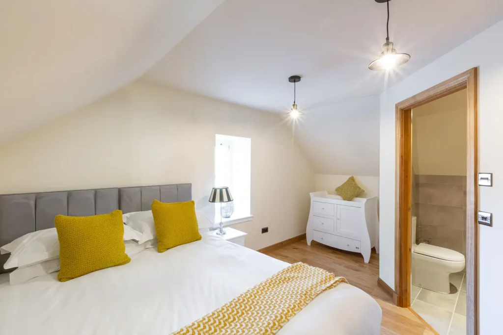 Cozy bedroom with yellow accents, plush bedding, modern lighting, and an en-suite bathroom in a minimalist design.