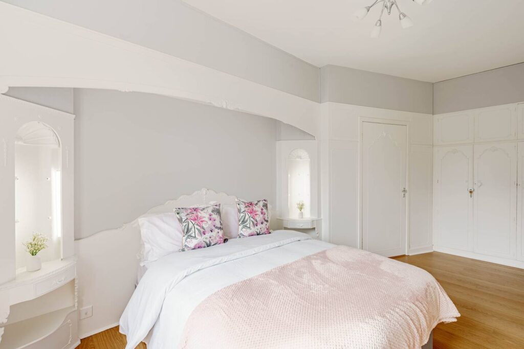 Elegant bedroom with pastel decor, floral pillows, and white cabinetry, creating a serene and inviting space.