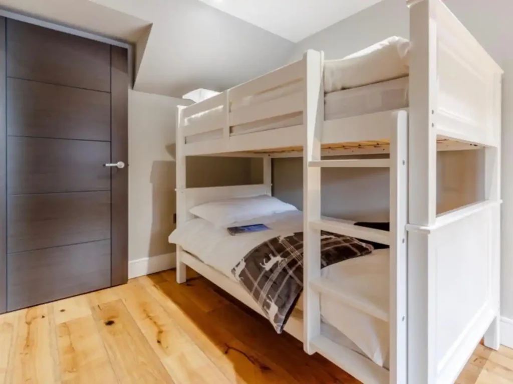 White bunk bed in a cozy room with wooden flooring and a modern door. Ideal space-saving solution for small bedrooms.