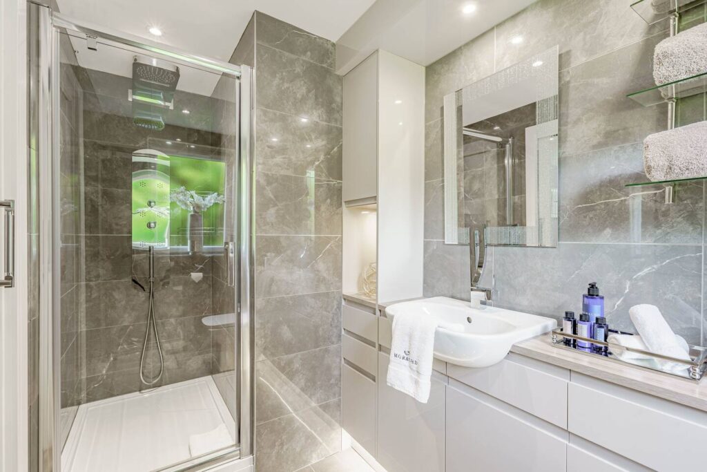 Modern bathroom with glass shower, sleek vanity, and luxury toiletries. Elegant grey tiles create a sophisticated look.