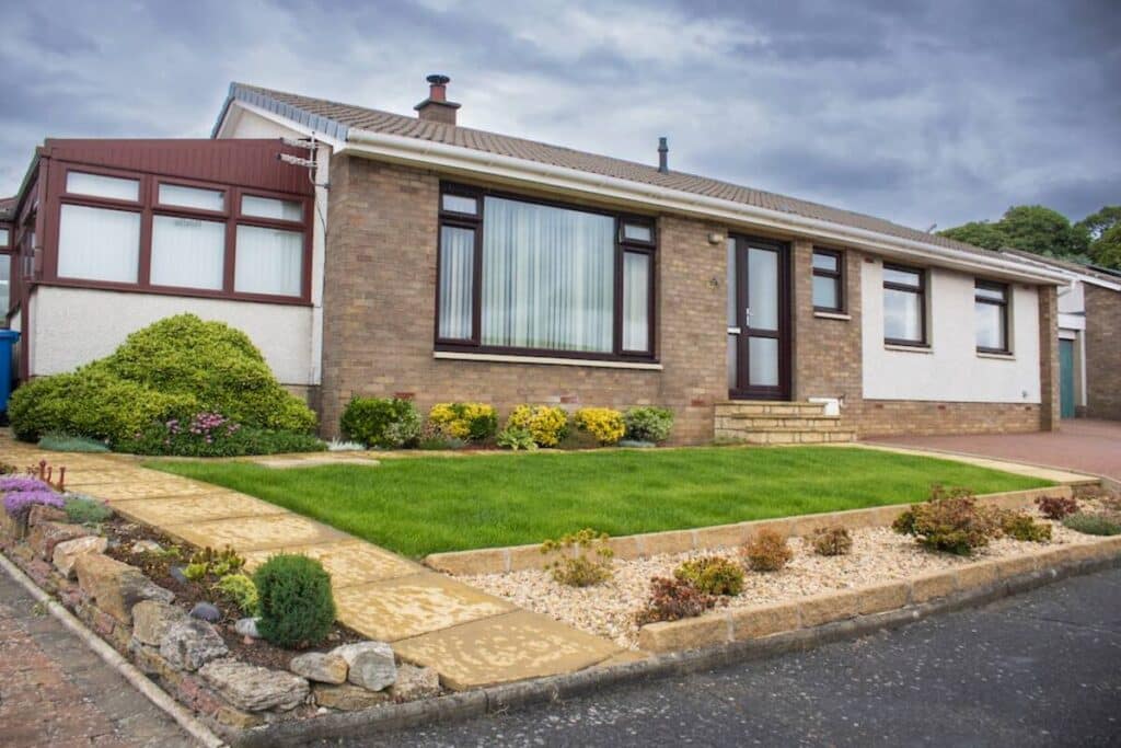 Single-story brick house with well-manicured lawn and landscaping, under a cloudy sky.