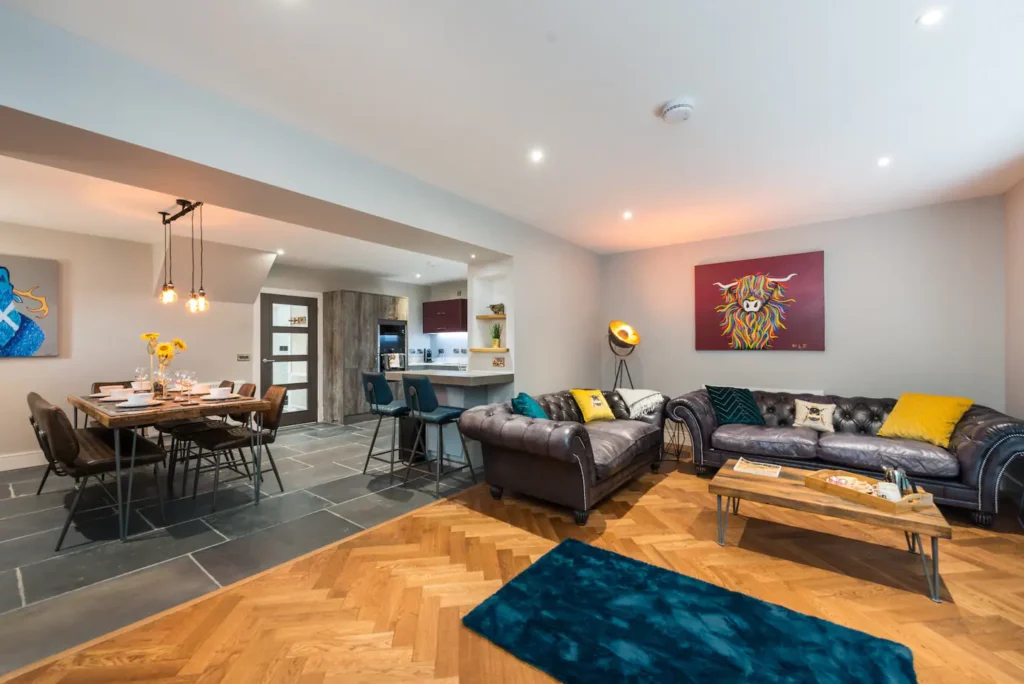 Modern open-plan living room with leather sofas, vibrant artwork, and dining area with rustic table and chairs.