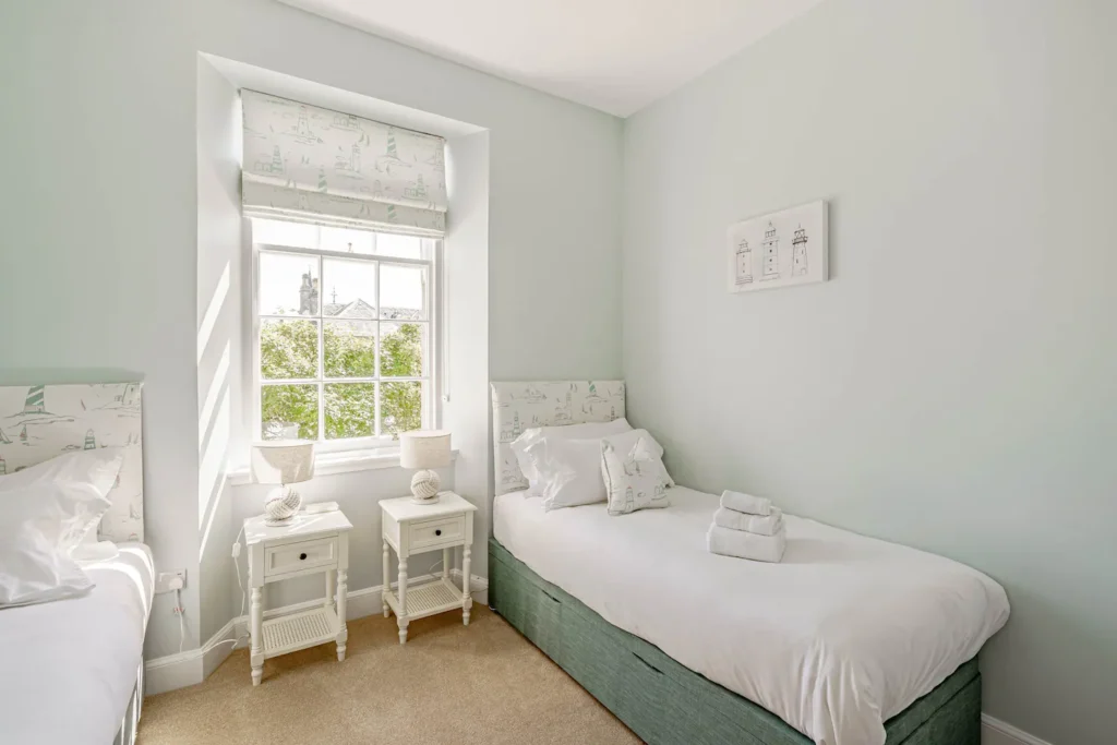 Cozy bedroom with twin beds, white nightstands, and a bright window view. Ideal for a peaceful and relaxing stay.