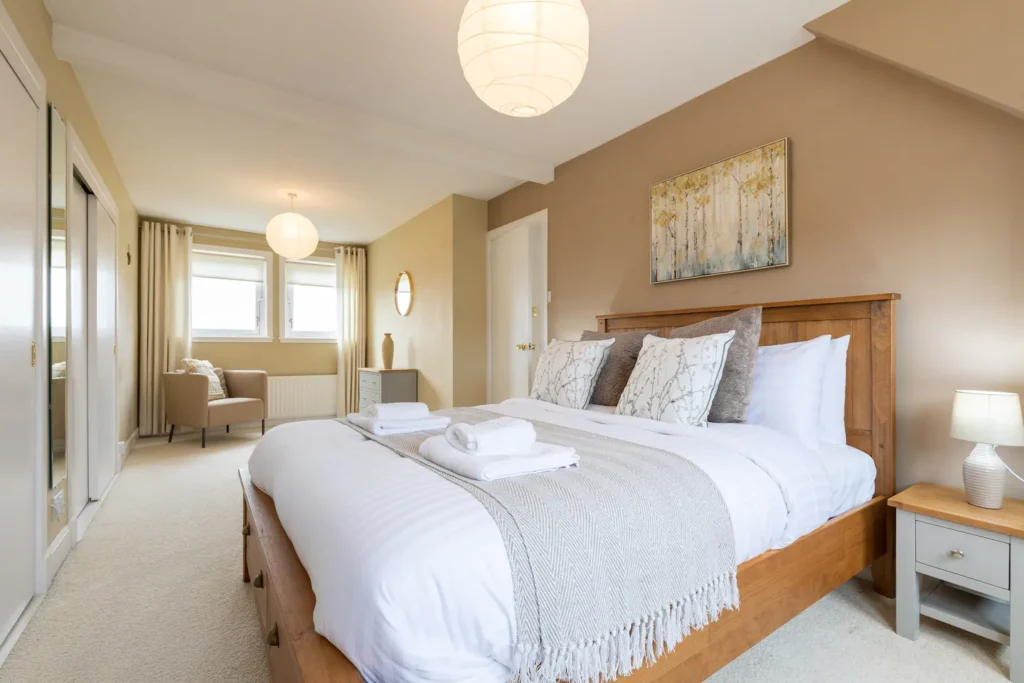 Cozy bedroom with wooden bed, white linens, and soft lighting in a modern, neutral-toned design.