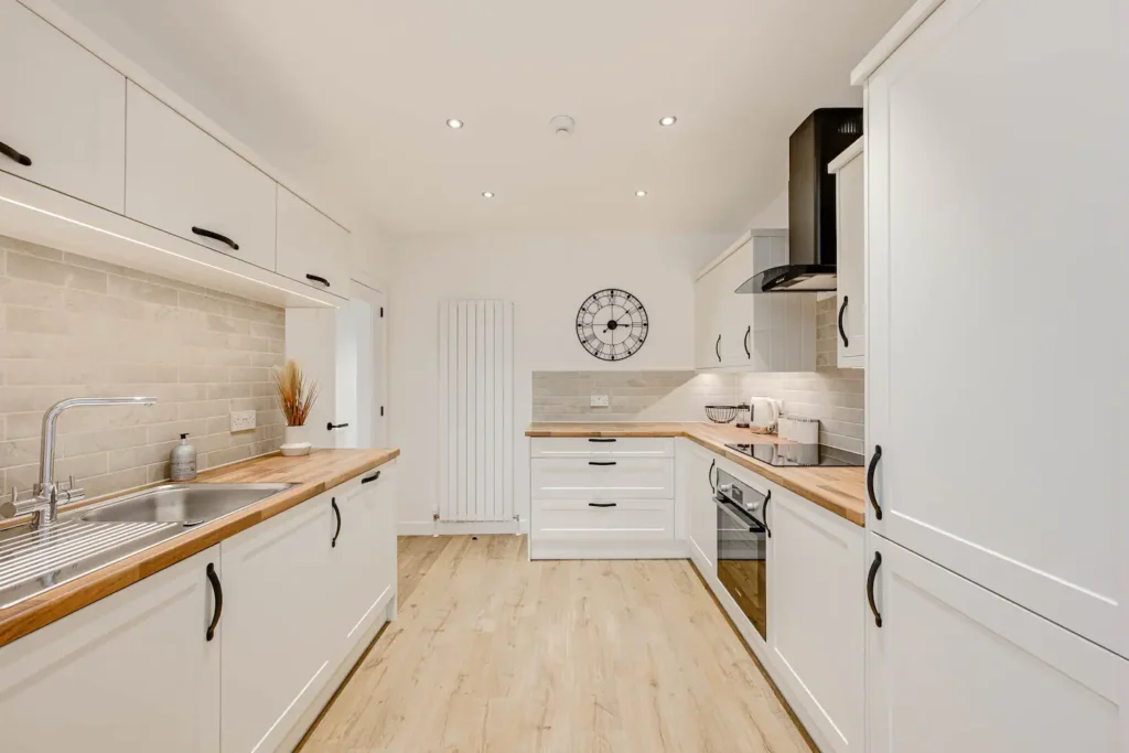 Modern white kitchen with wooden countertops, sleek appliances, and wall clock. Bright and minimalist design.