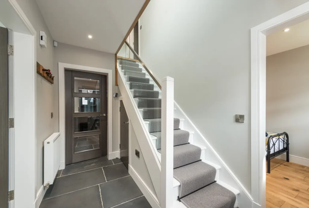 Modern hallway with carpeted stairs, glass railing, and gray door. Stylish, minimalist interior design.