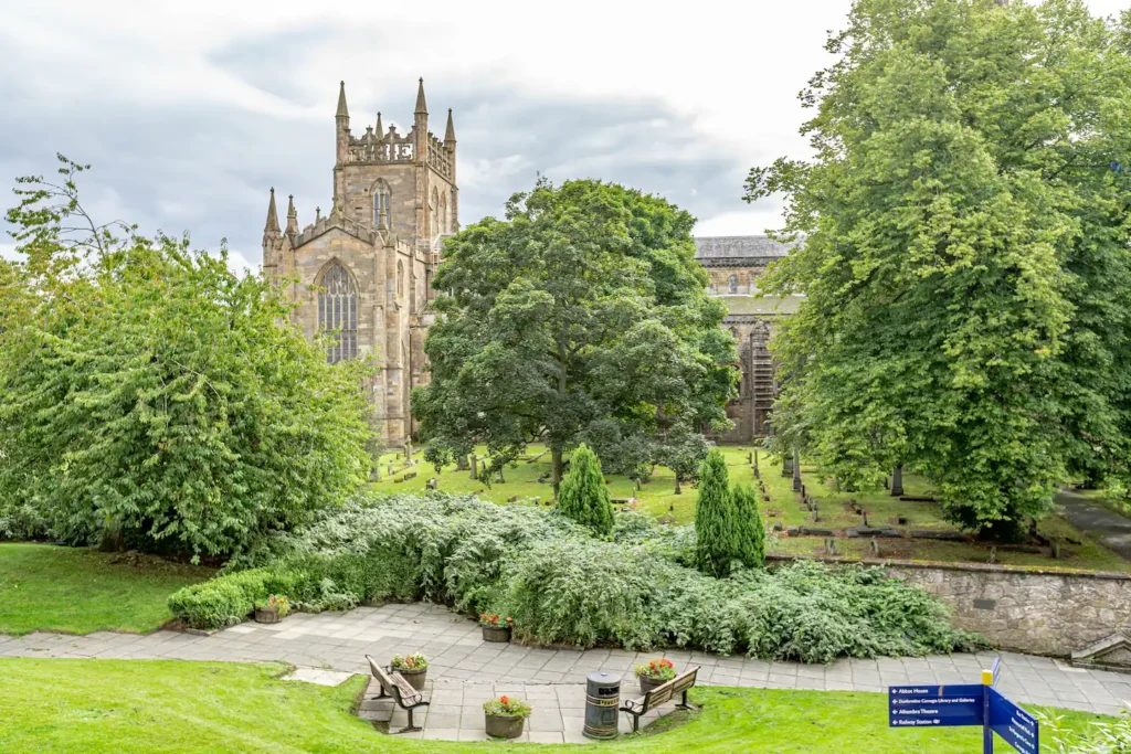 Historic stone church with greenery and benches in a peaceful garden setting under a cloudy sky.