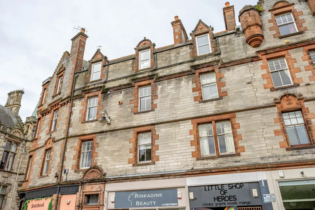 Historic building facade with shops in Dunfermline, featuring brick details and large windows.