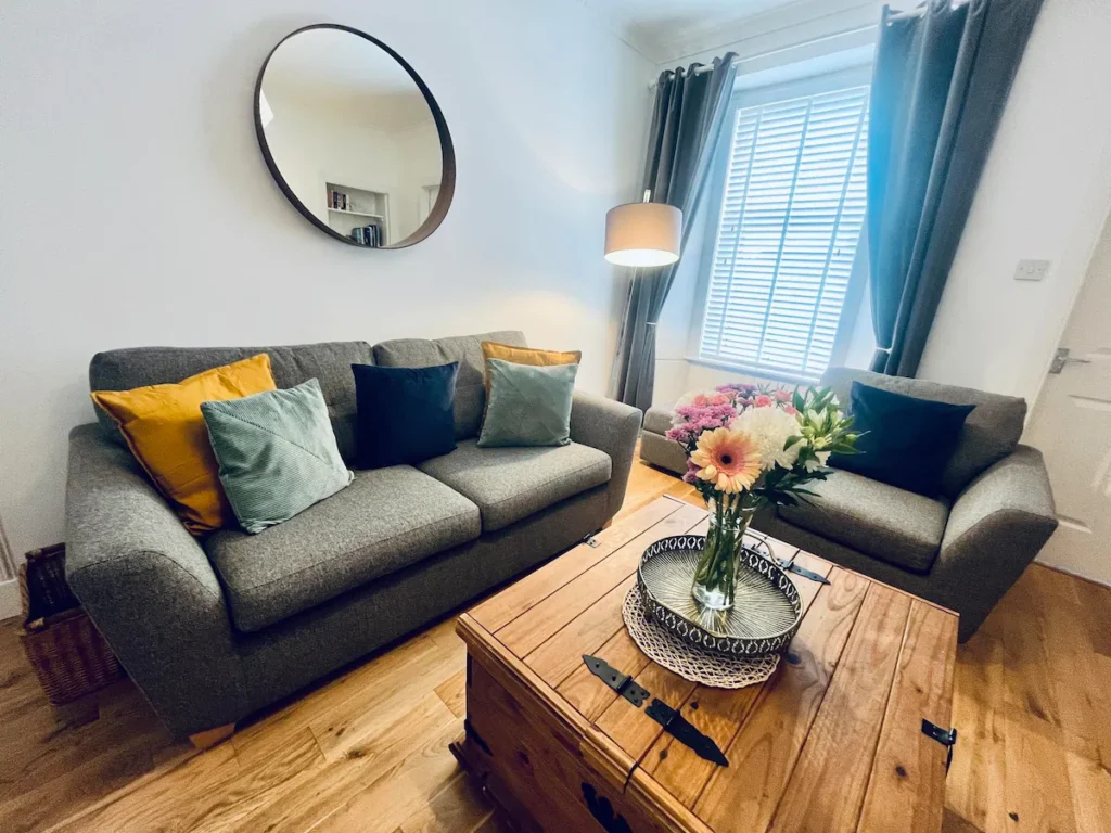 Cozy living room with grey sofas, colorful cushions, wooden table, and a large wall mirror for a modern home feel.