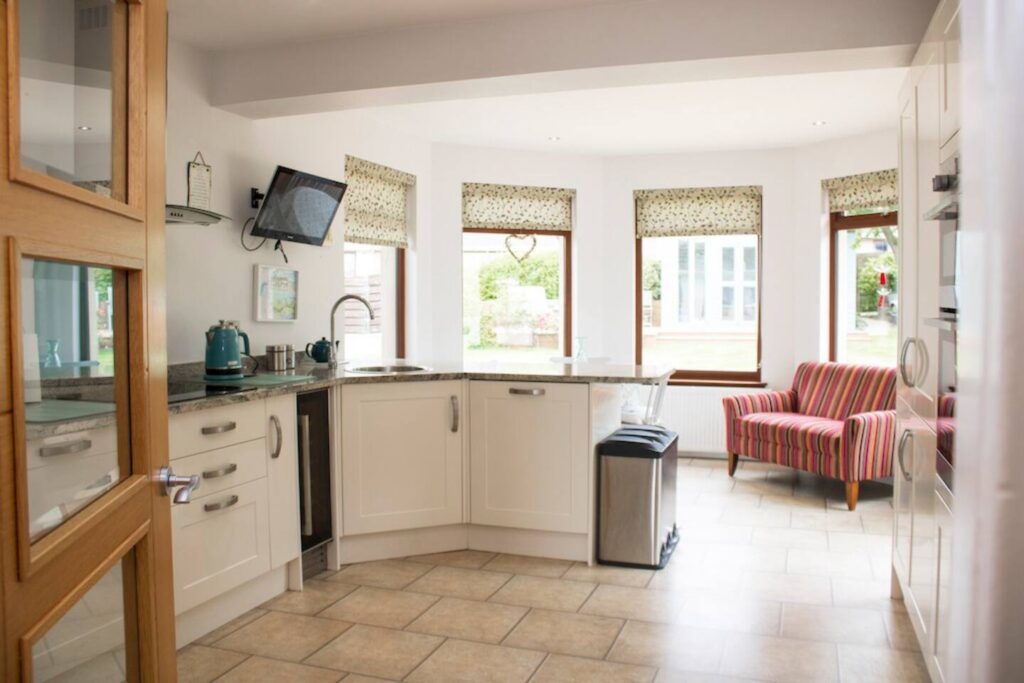 Bright modern kitchen with white cabinets, granite countertops, and a cozy striped armchair by the windows.