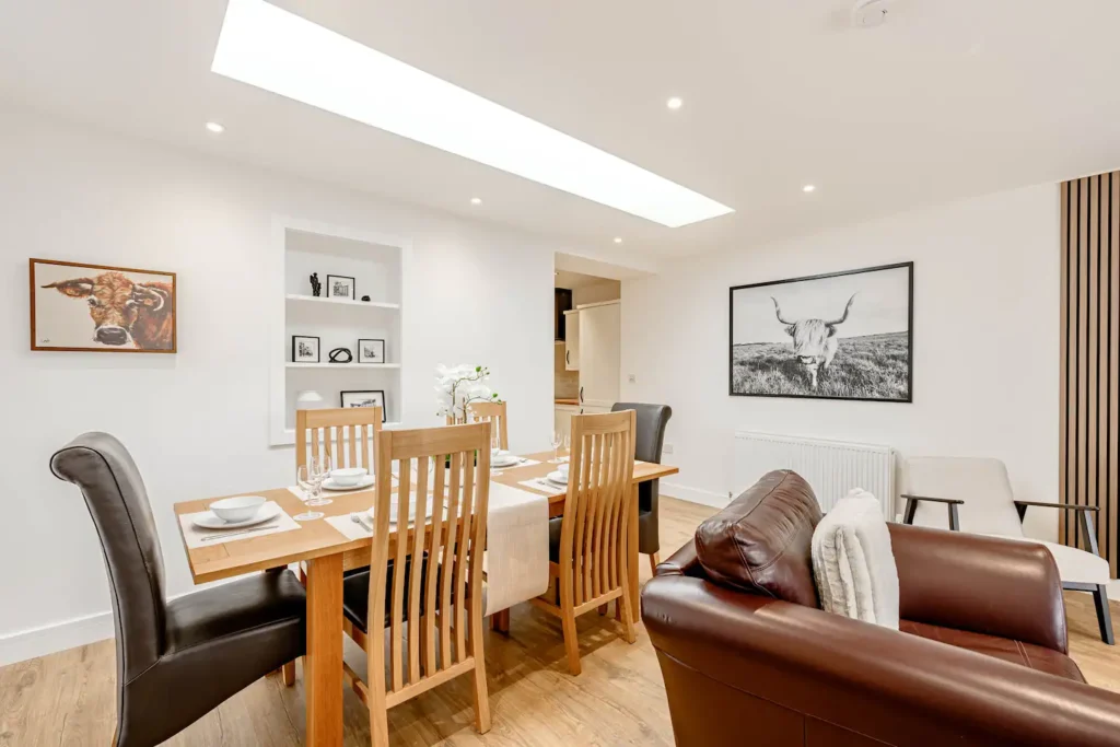 Modern dining area with wooden table, chairs, and cow artwork on white walls, featuring cozy leather seating.