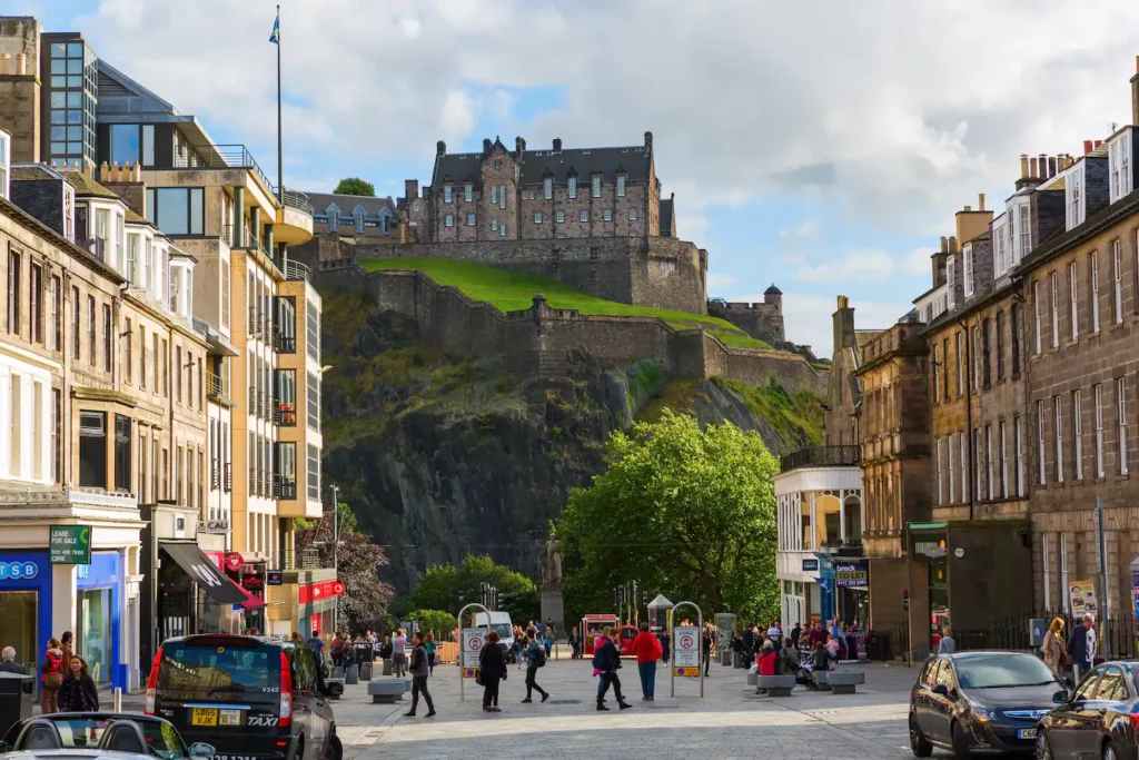 Street view of Edinburgh with bustling tourists and the iconic Edinburgh Castle in the background.