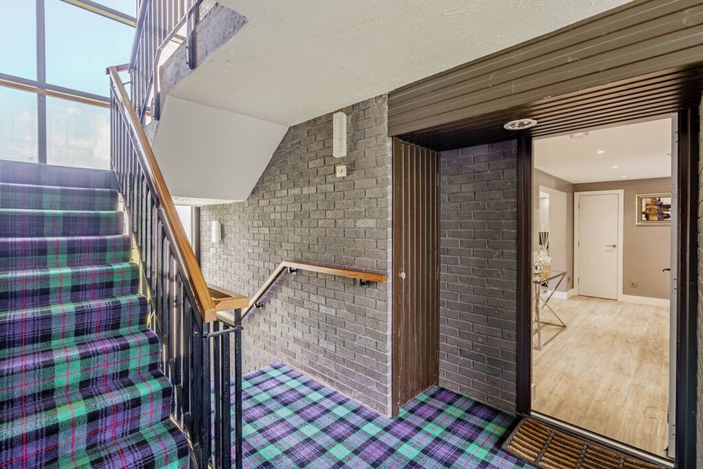 Modern stairway with colorful tartan carpet and open door leading to bright, stylish interior space.