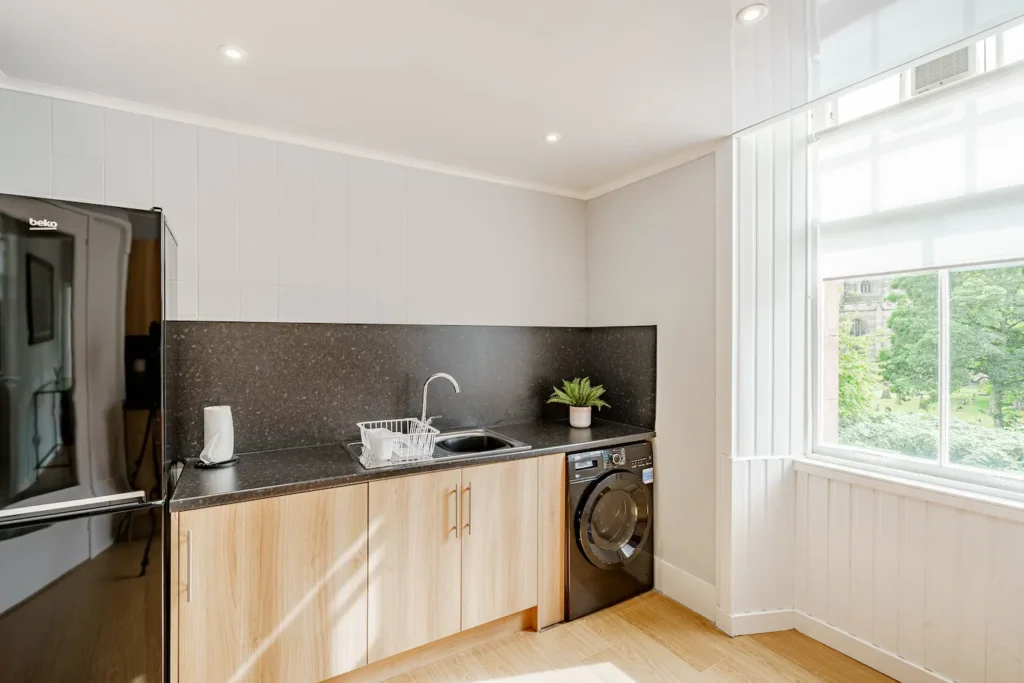 Modern kitchen with wood cabinets, black countertop, sink, washing machine, and large window with scenic view.