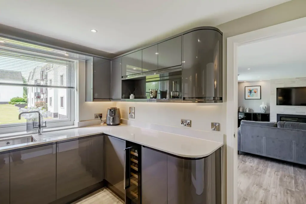 Modern kitchen with sleek gray cabinets, white countertops, and a window view, opening into a stylish living room.