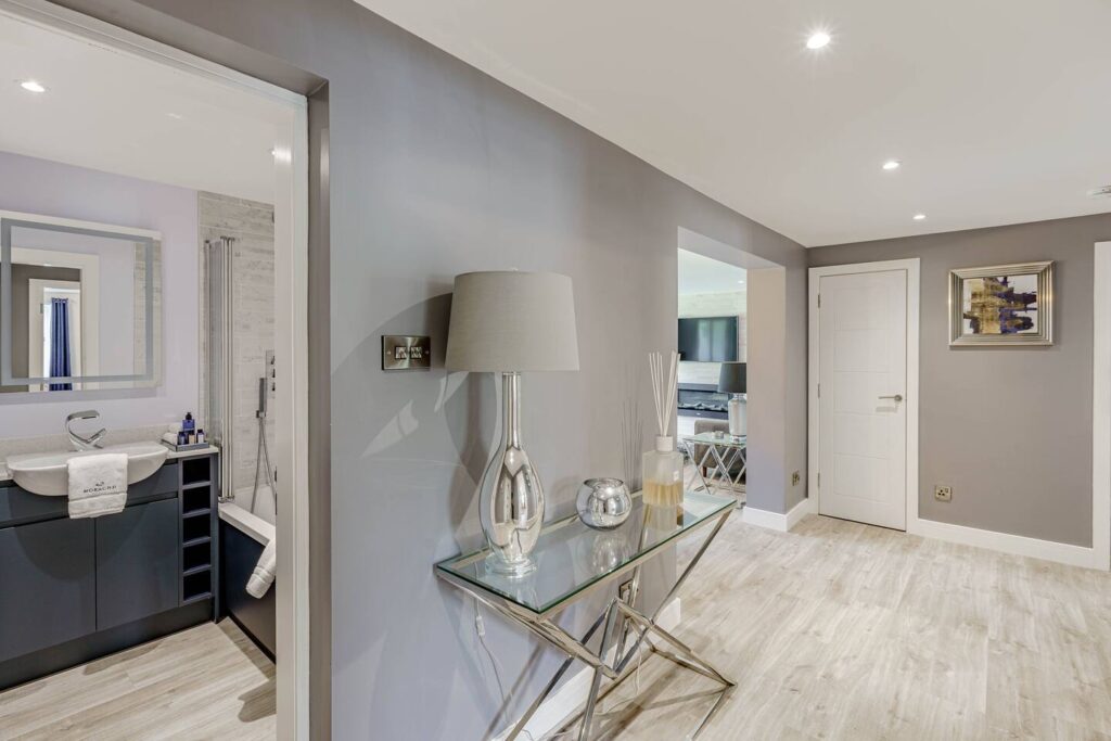 Modern gray hallway with console table, lamp, and view into bathroom and living room. Elegant home interior design.