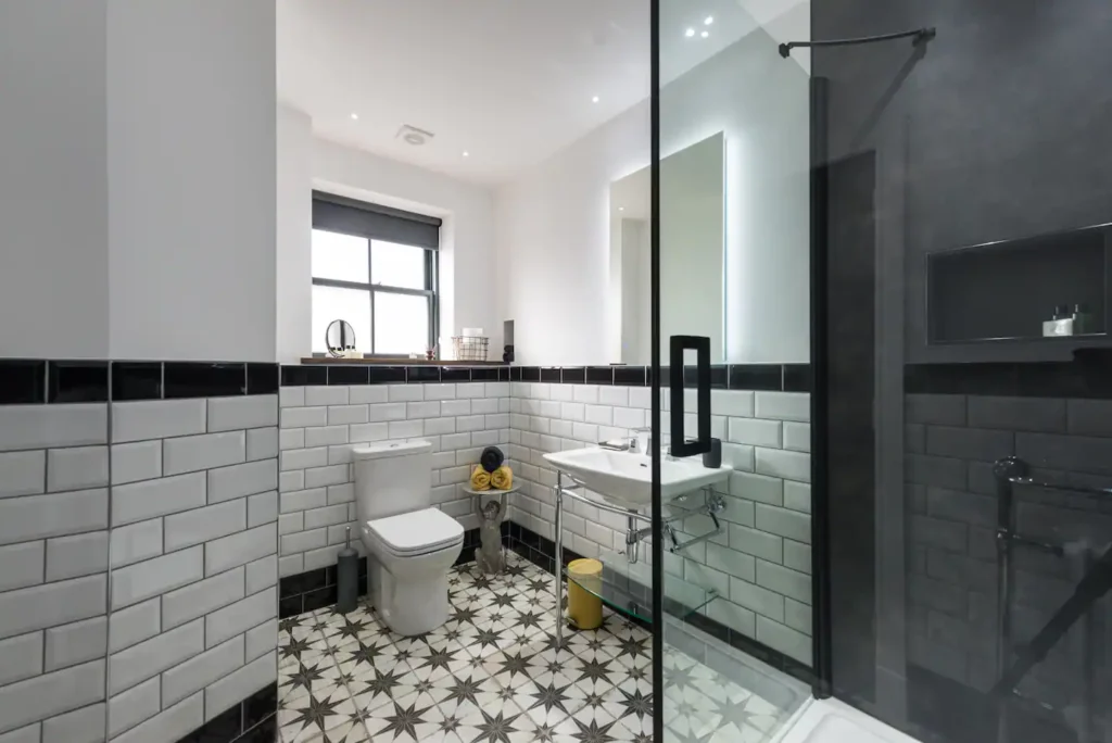 Modern bathroom with black and white tiles, glass shower, and elegant fixtures.