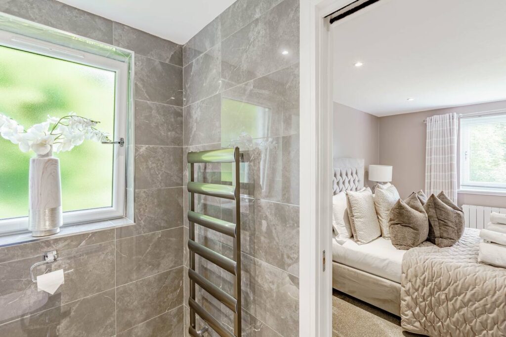 Cozy bedroom with plush pillows, adjacent to a modern bathroom with tiled walls and frosted window.